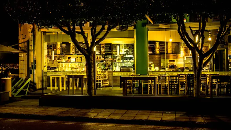 A small café on a city street at night, with warm lights on inside